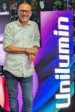 Ein Bild eines Mitarbeiters der Unilumin Germany GmbH. Der Mann steht in Jeans und Hemd bekleidet vor einer LED-Wand die das Logo der Unternehmung zeigt.